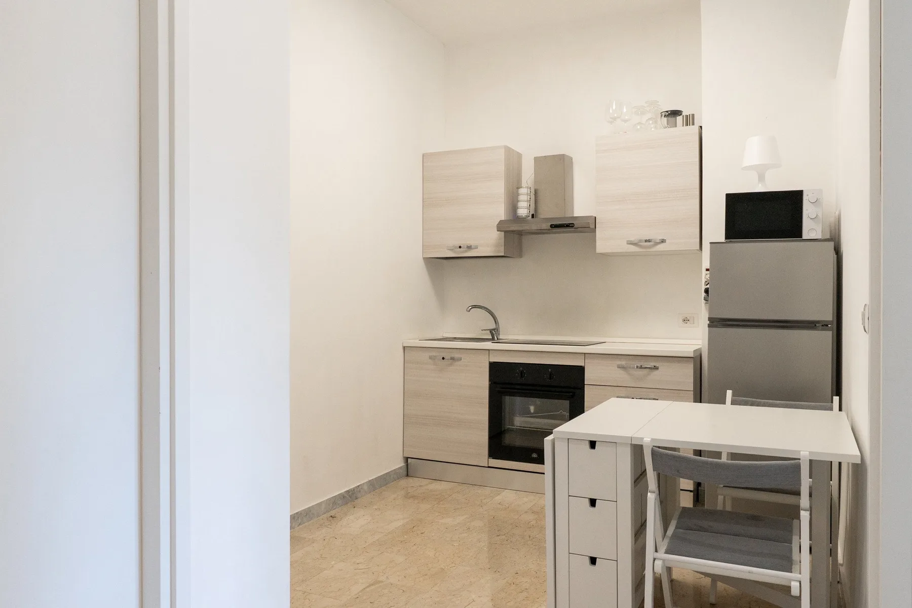 A compact kitchen with light cabinets, a refrigerator, and a small dining table.