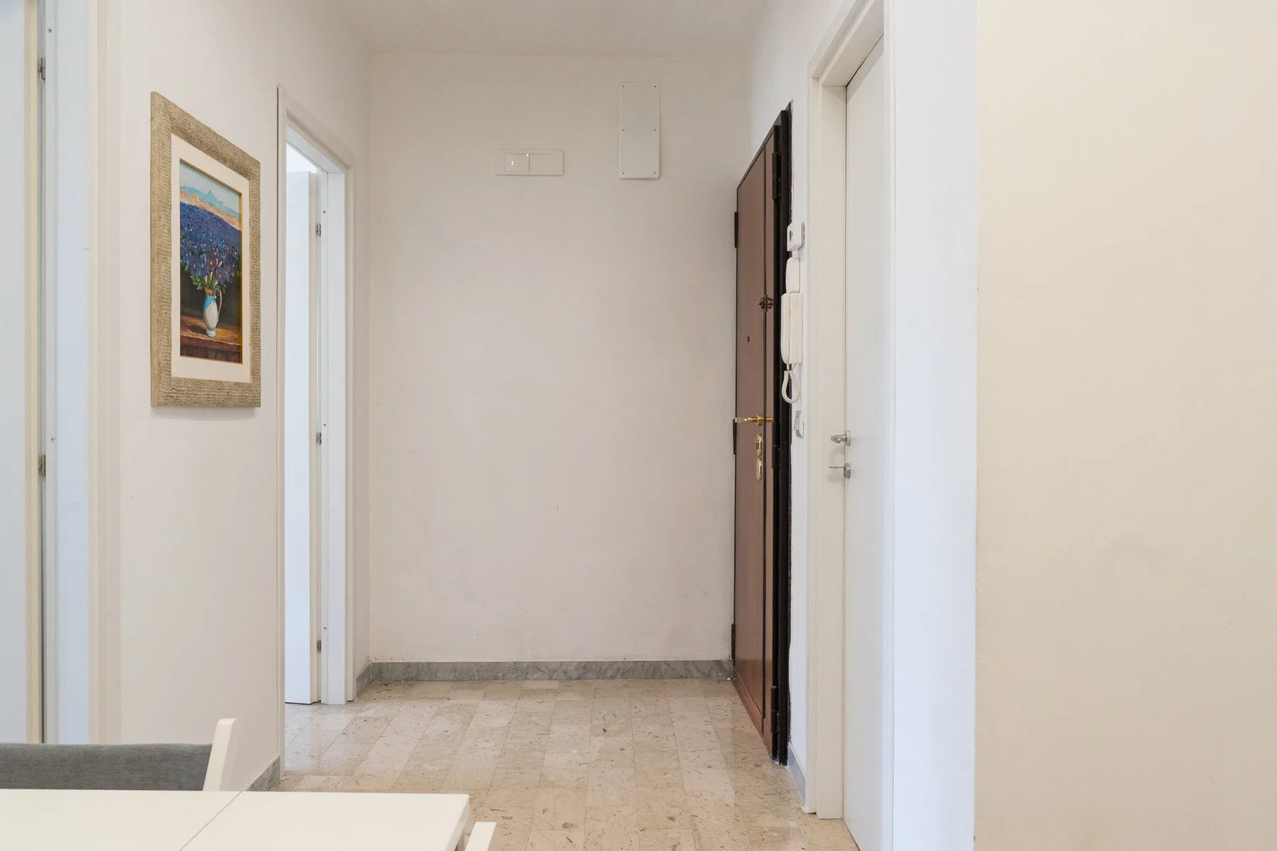 A bright hallway with light stone flooring and framed wall art.
