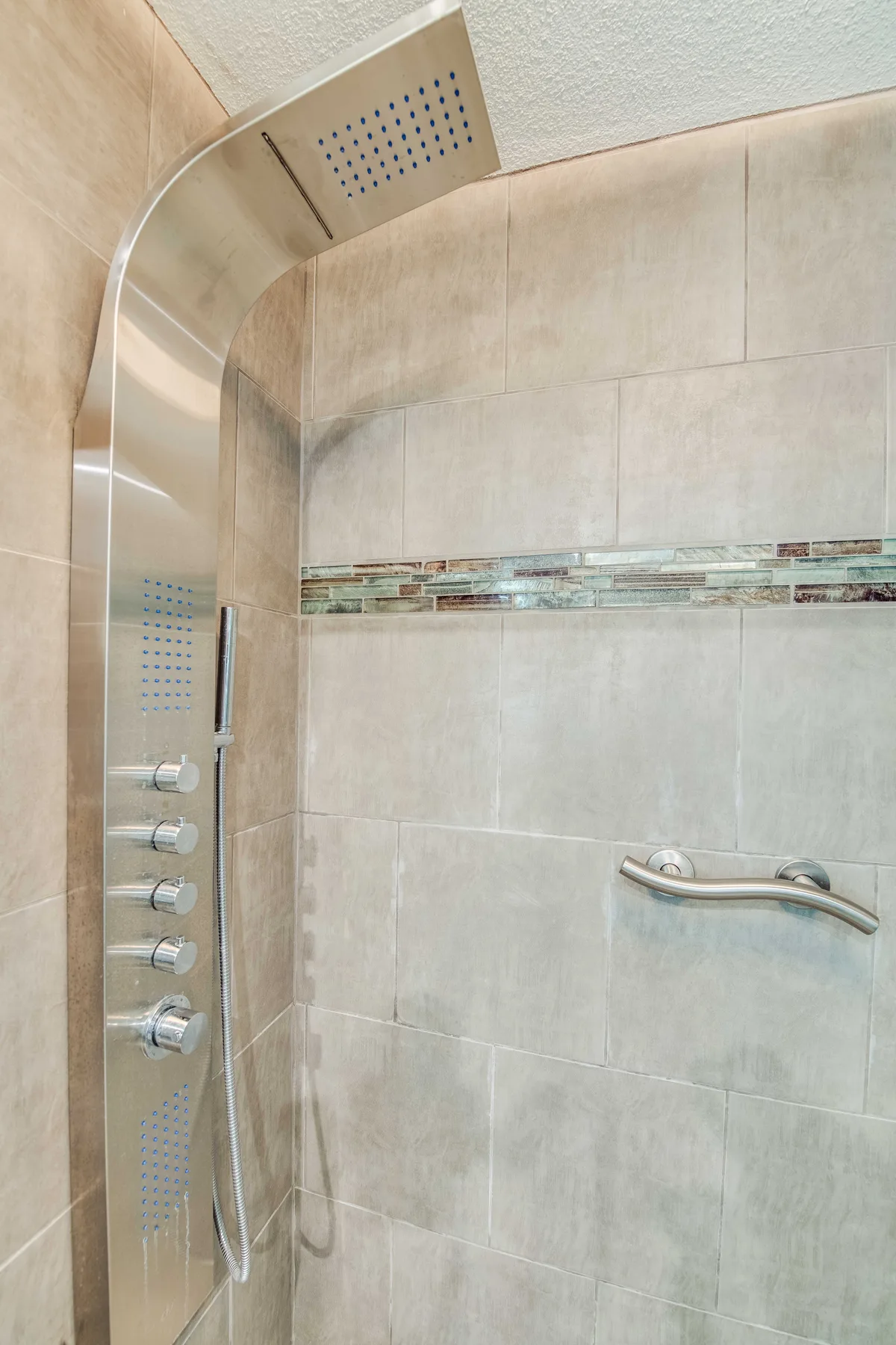 A tiled shower area with a large overhead shower fixture and wall-mounted controls.