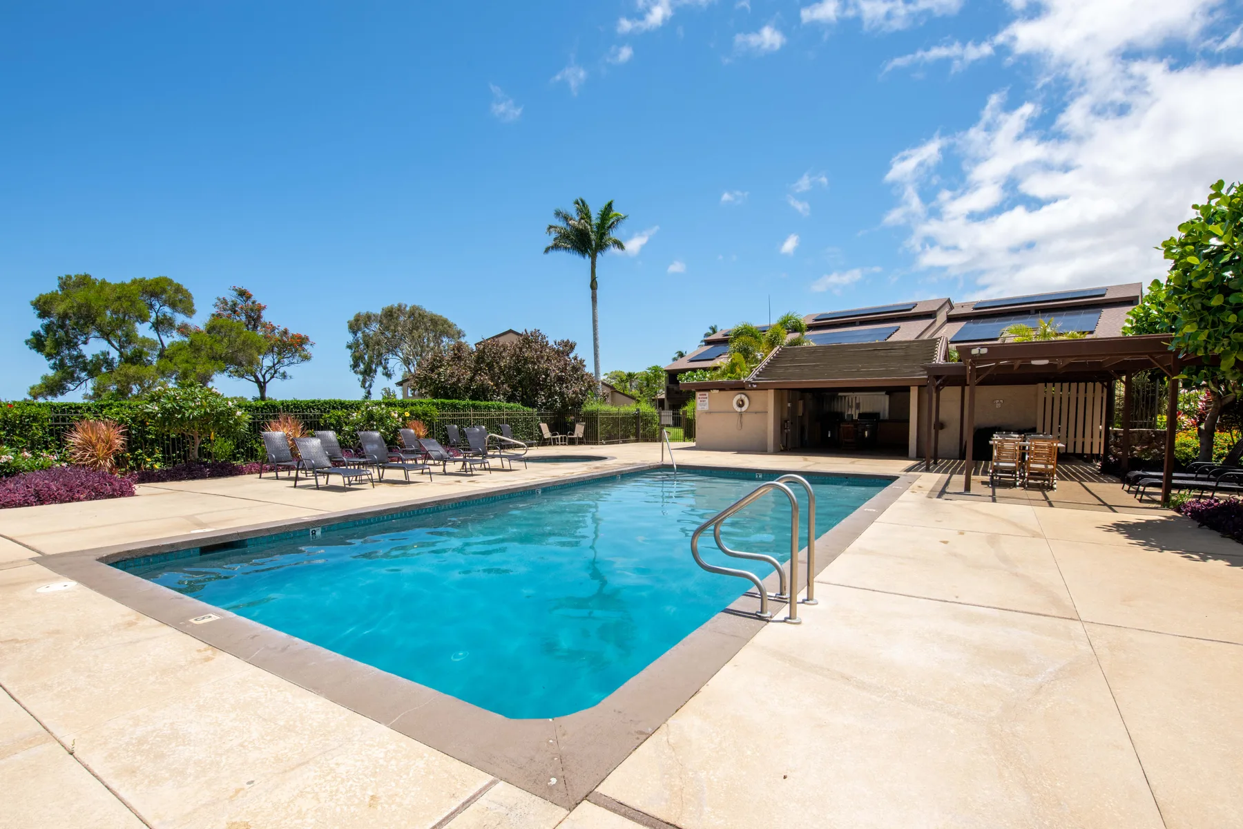 Outdoor swimming pool beside a covered patio, with lounge seating and greenery.