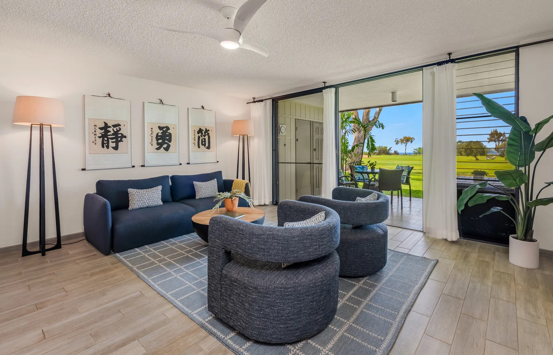A living room with seating arranged around a low table beside open sliding glass doors.
