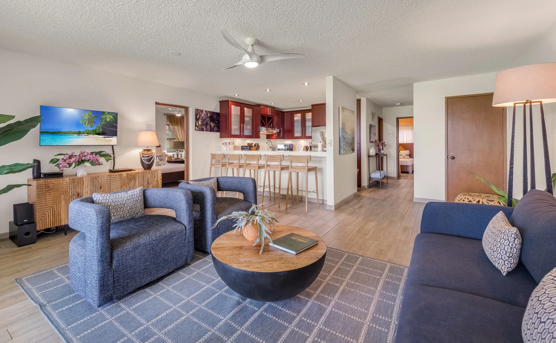 A living room with blue seating and an open kitchen beyond.