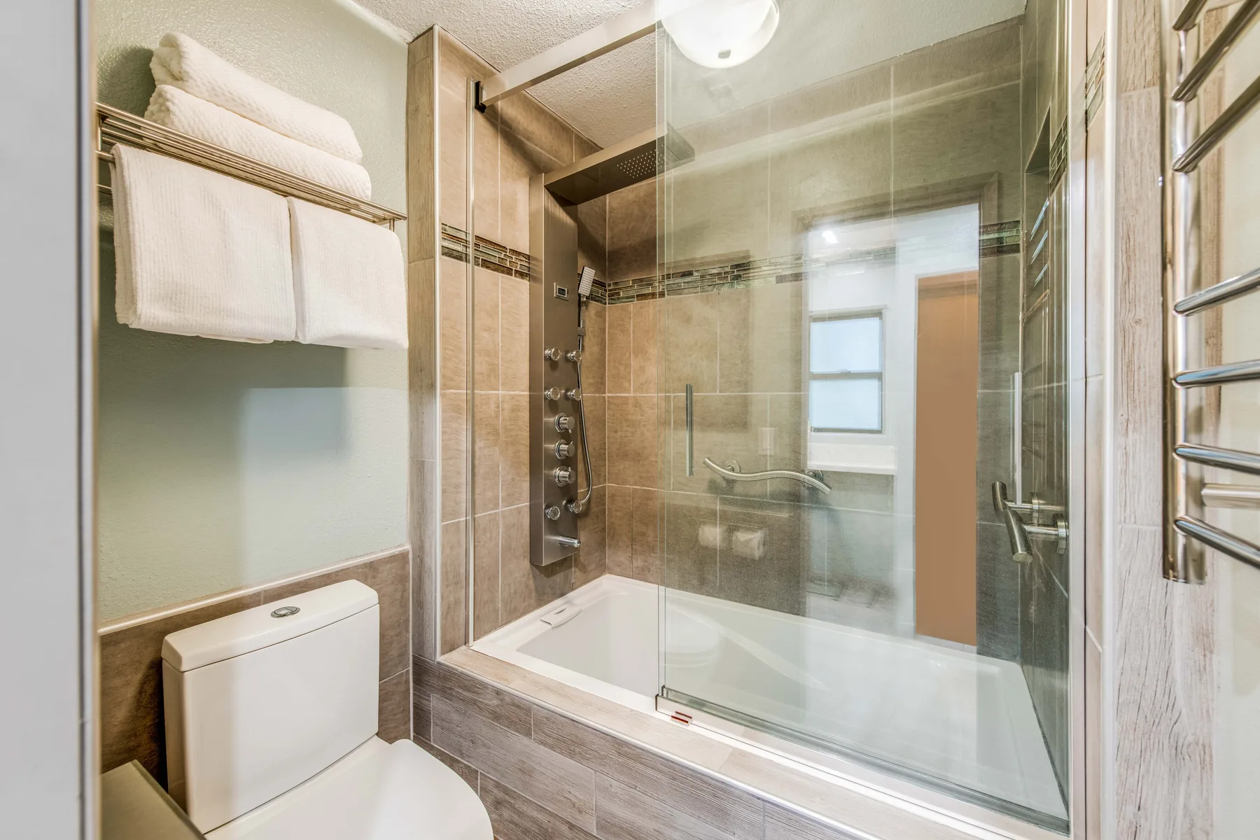 A bathroom with a glass-enclosed shower and towels on a wall rack.