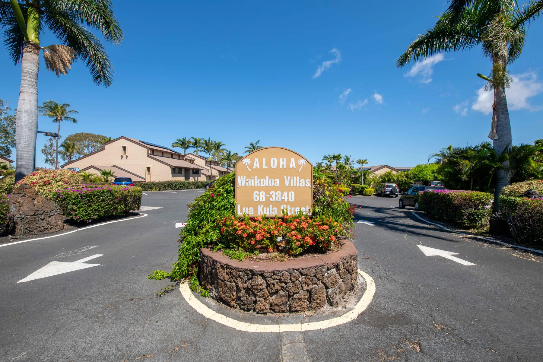 A landscaped entrance island with a flower bed and sign sits between paved driveways.