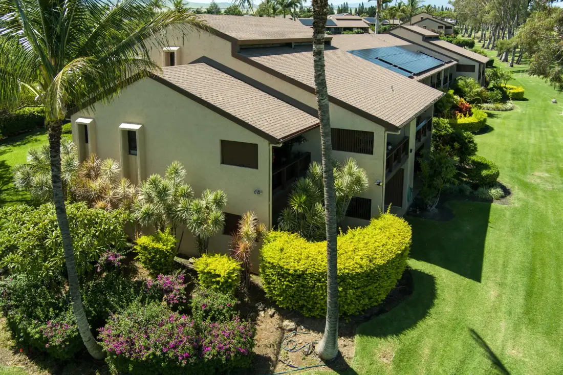 A landscaped residential building with sloped roofs sits among palm trees and green lawns.