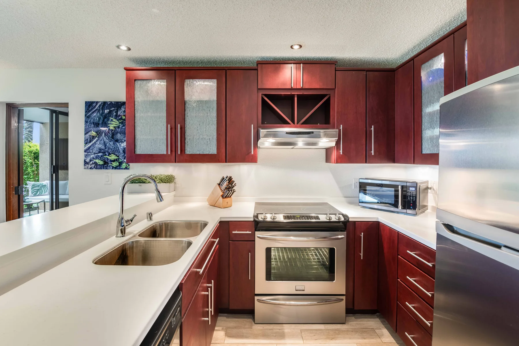 A modern kitchen with dark red cabinetry, light countertops, and stainless steel appliances.