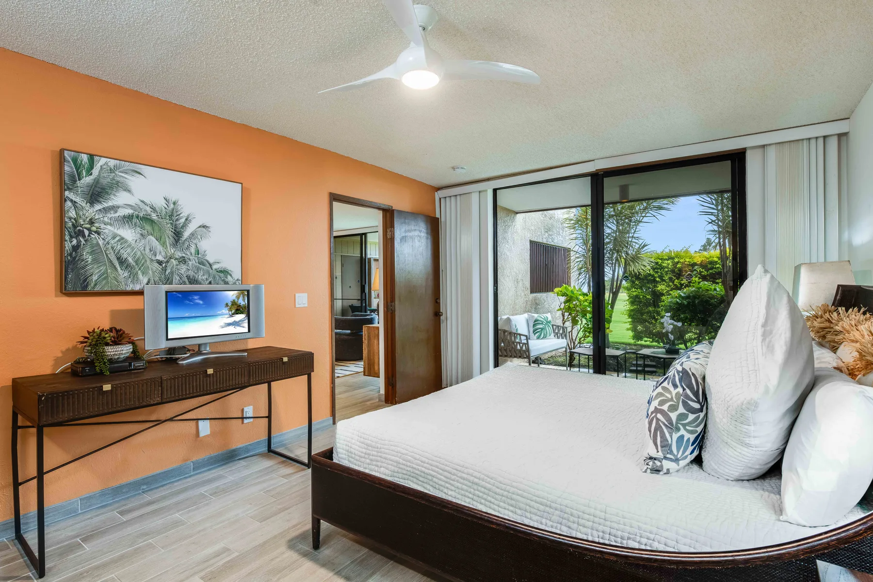 A bedroom with a large bed, a desk, and sliding glass doors opening to a garden.