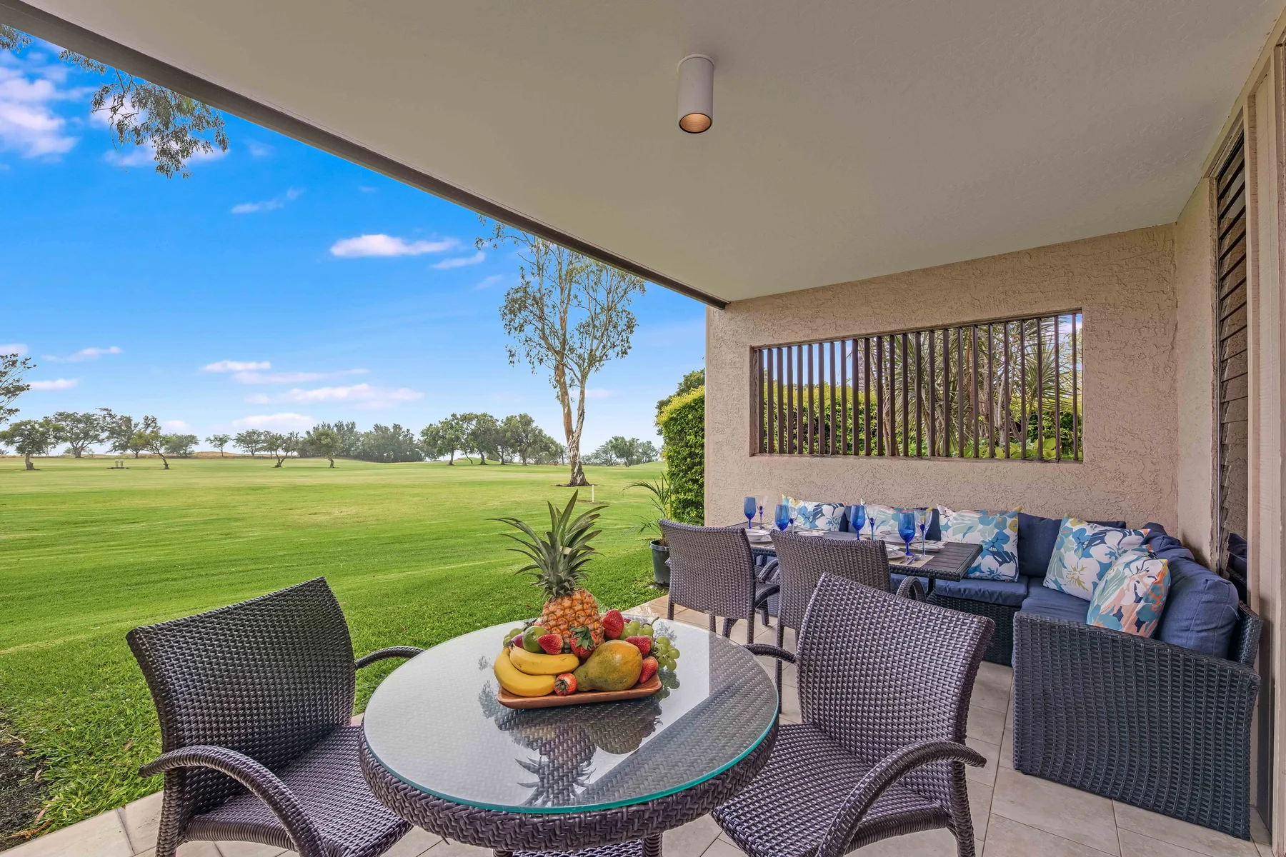 A covered patio has seating around a table overlooking a broad green lawn.