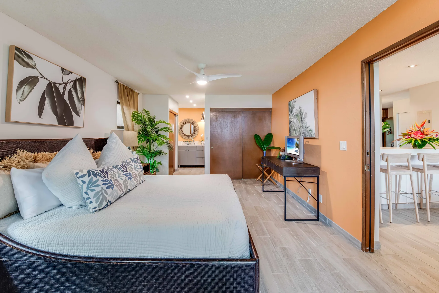 A bedroom with a large bed, a television, and an open doorway to a dining area.