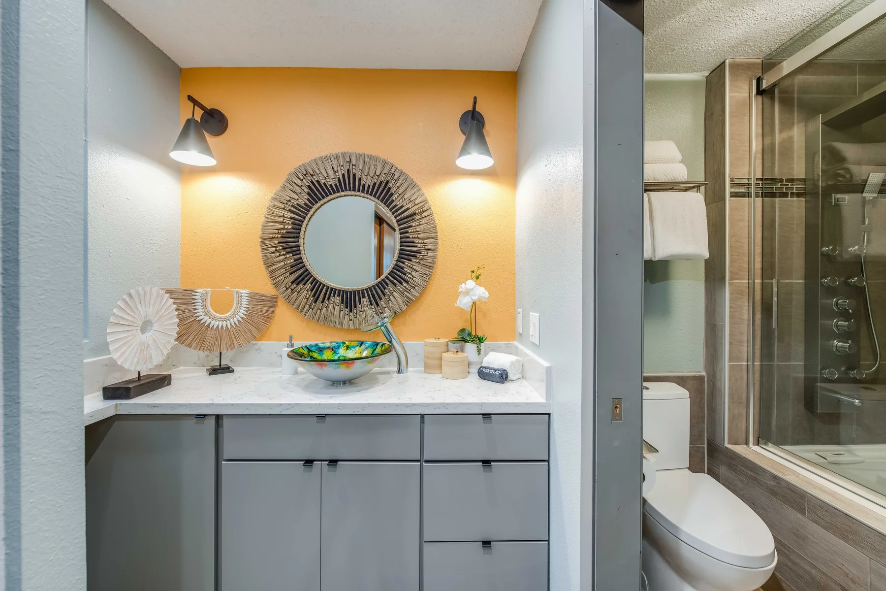 A bathroom vanity with a round mirror and a glass shower area.