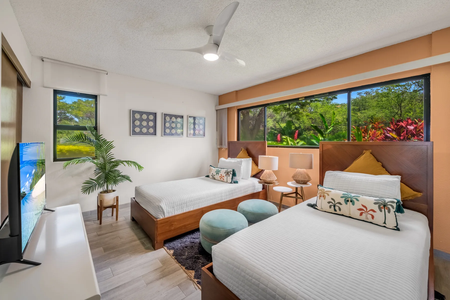 A bedroom with two beds, bedside lamps, and windows overlooking greenery.