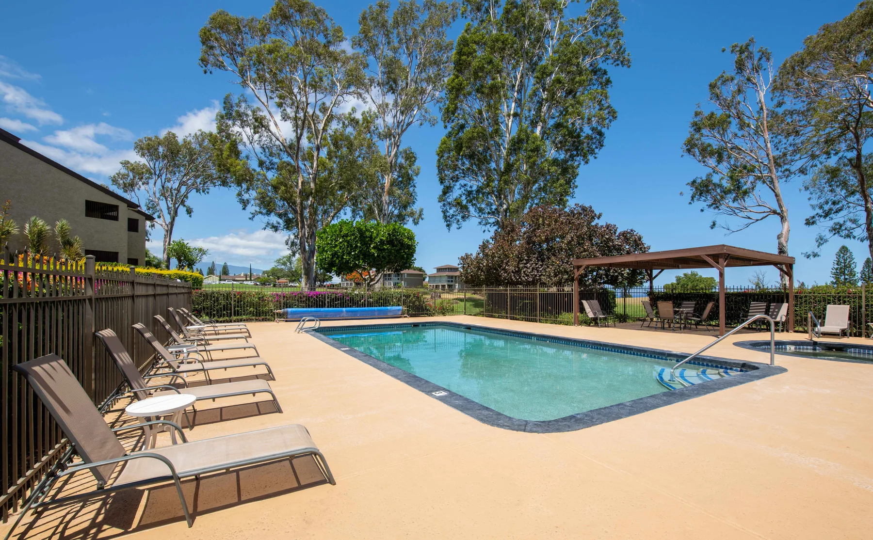 An outdoor swimming pool sits beside lounge seating and a shaded pergola.