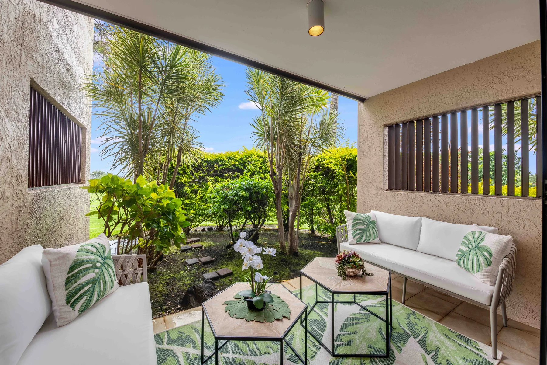 A covered patio with cushioned seating and a garden visible beyond.