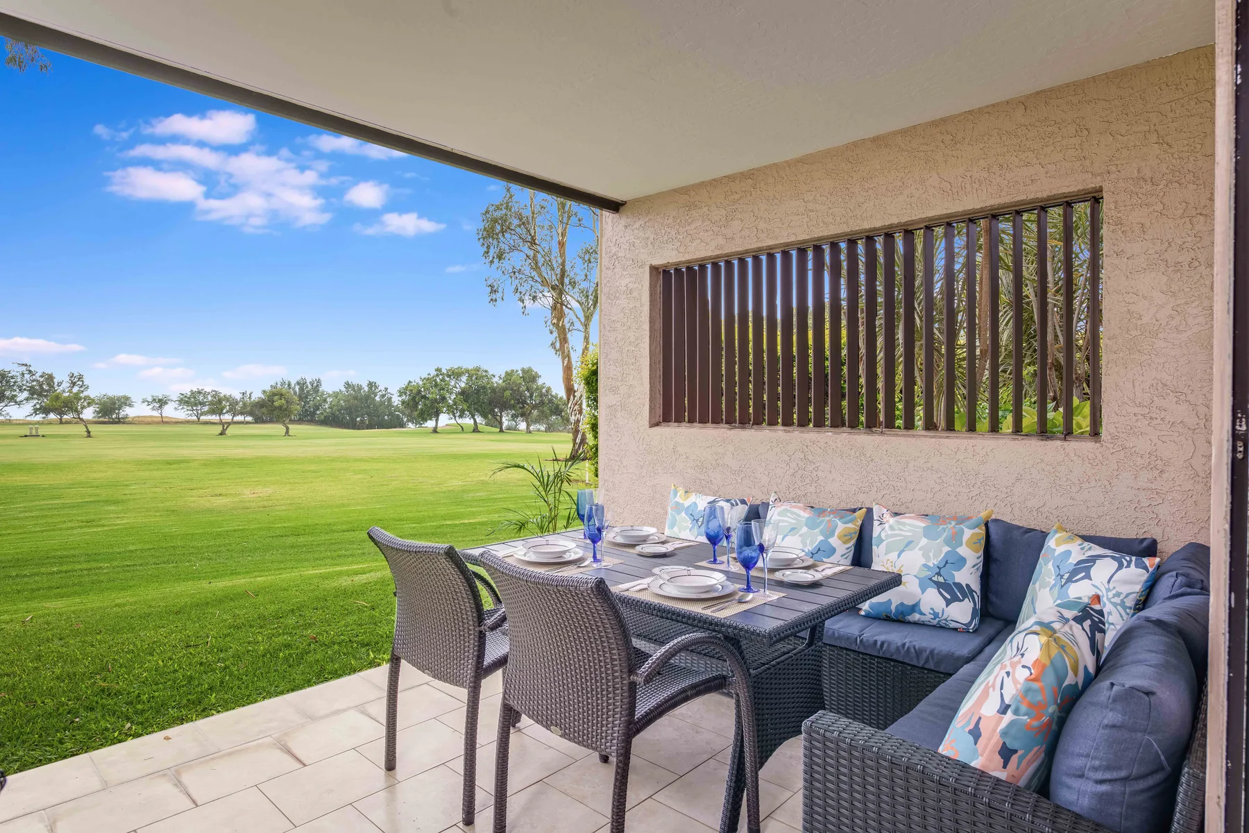 A covered patio has outdoor seating and a dining table overlooking a green lawn.