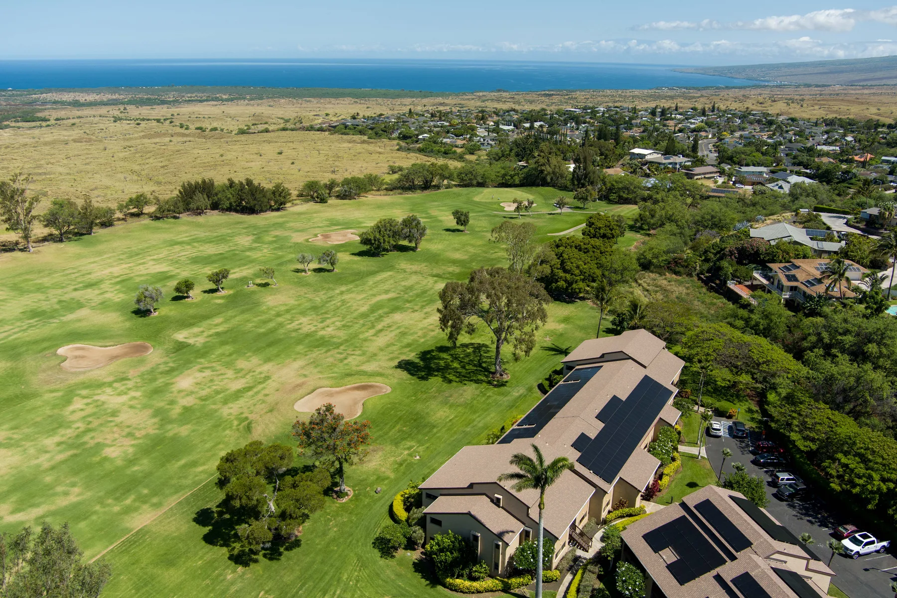 Aerial view of a golf course beside homes, with the ocean visible in the distance.