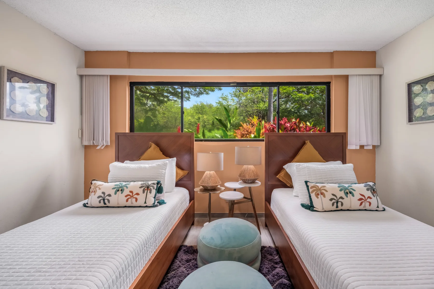 A bedroom with two single beds, bedside tables, and a wide window overlooking greenery.