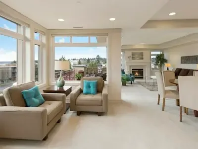 Una sala luminosa con asientos junto a grandes ventanas y un comedor.