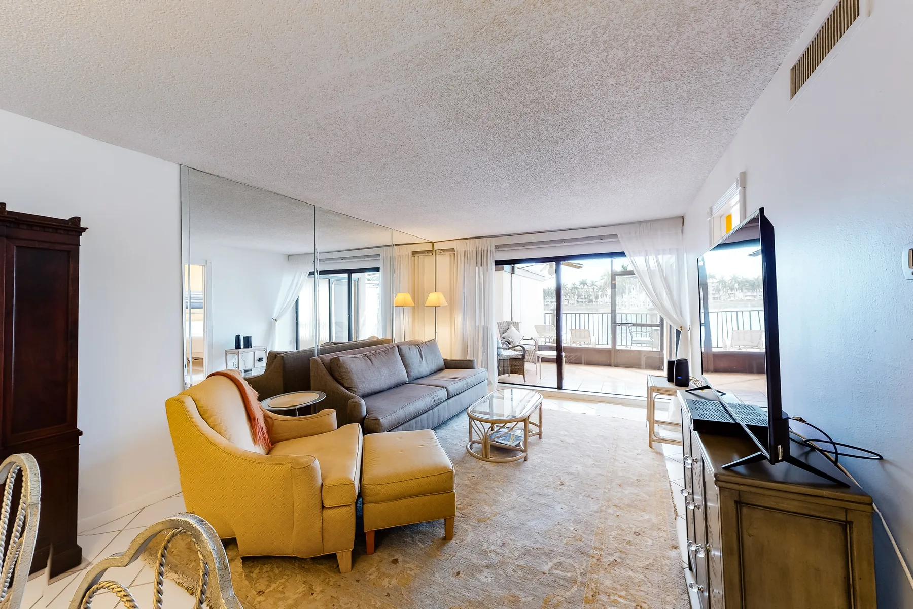 A living room with a sectional sofa, armchair, and television beside the windows.
