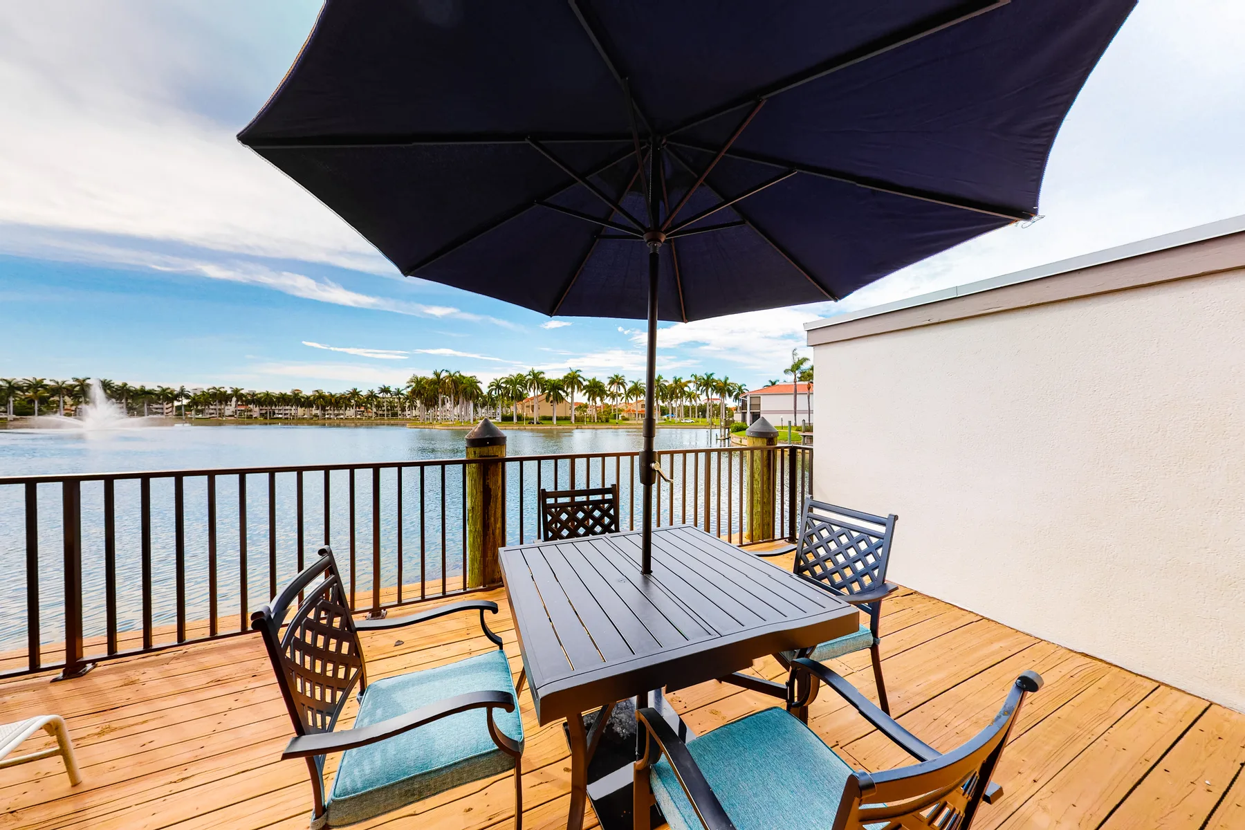 A waterfront deck has a dining table and seating beneath a large umbrella.