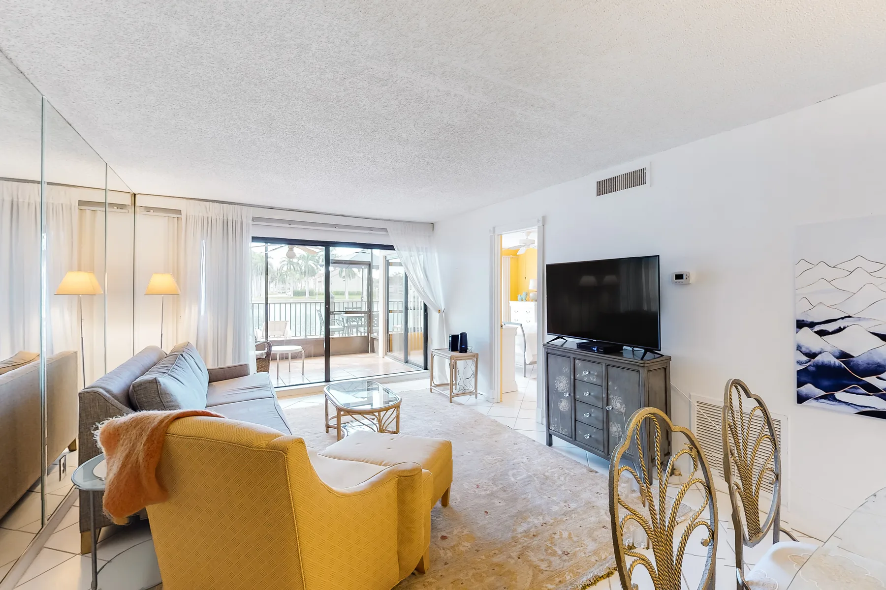 A bright living room with seating, a television, and glass doors opening to a balcony.
