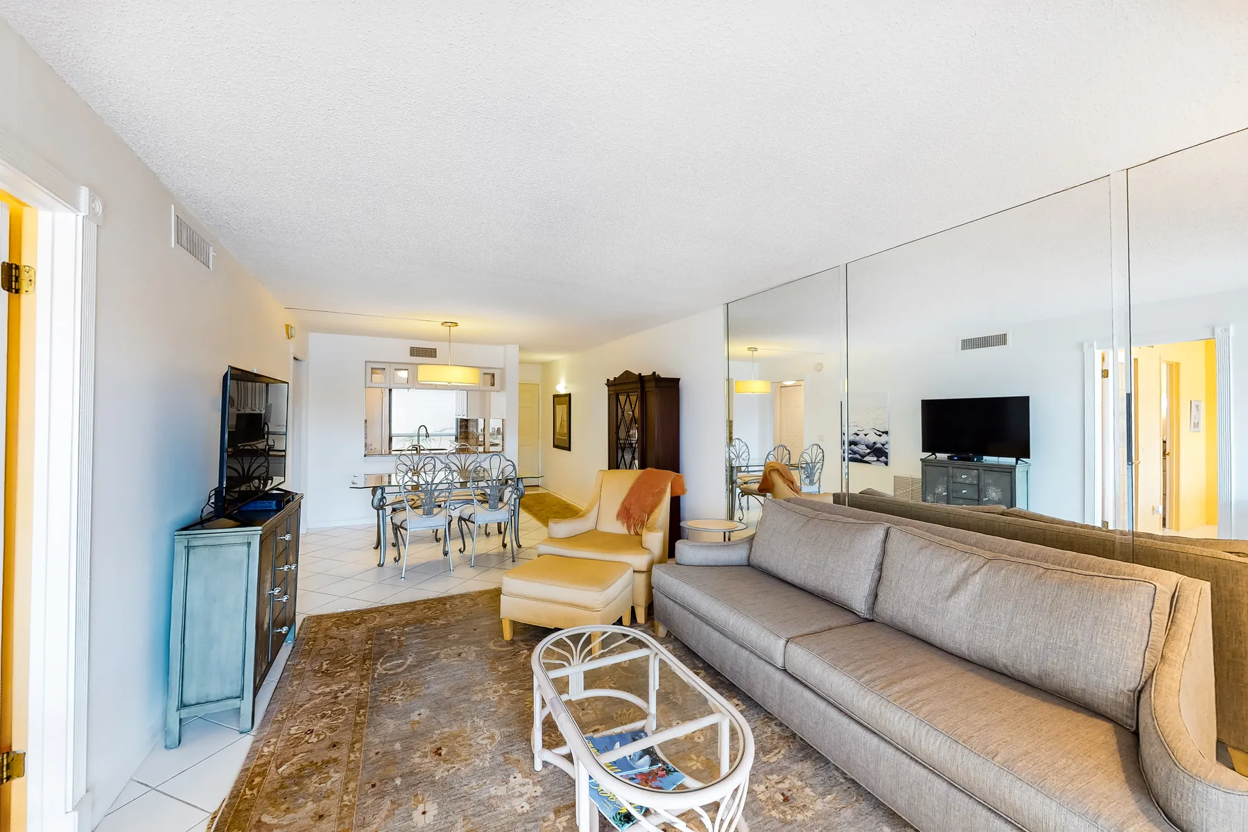 A living room with seating, a glass coffee table, and mirrored walls.