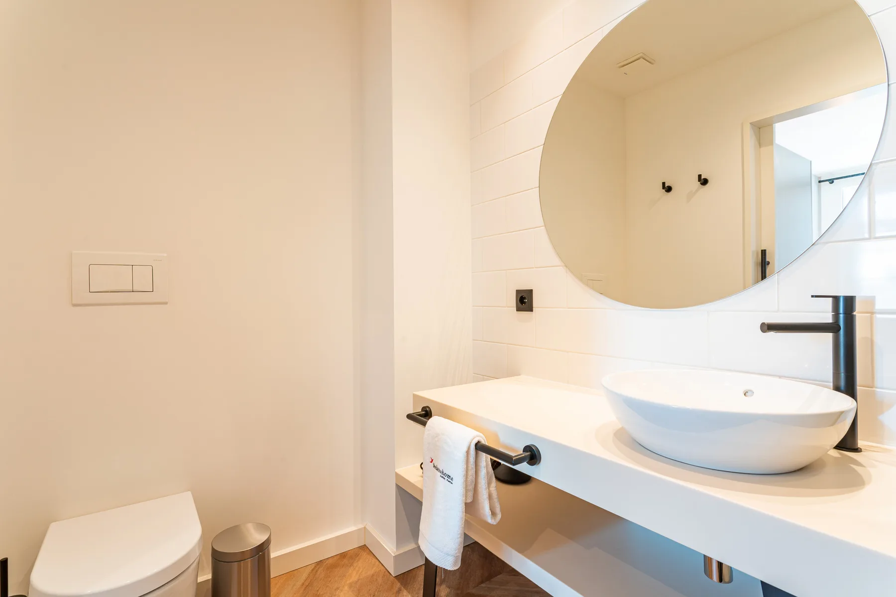 A bright bathroom with a sink, large round mirror, and toilet.