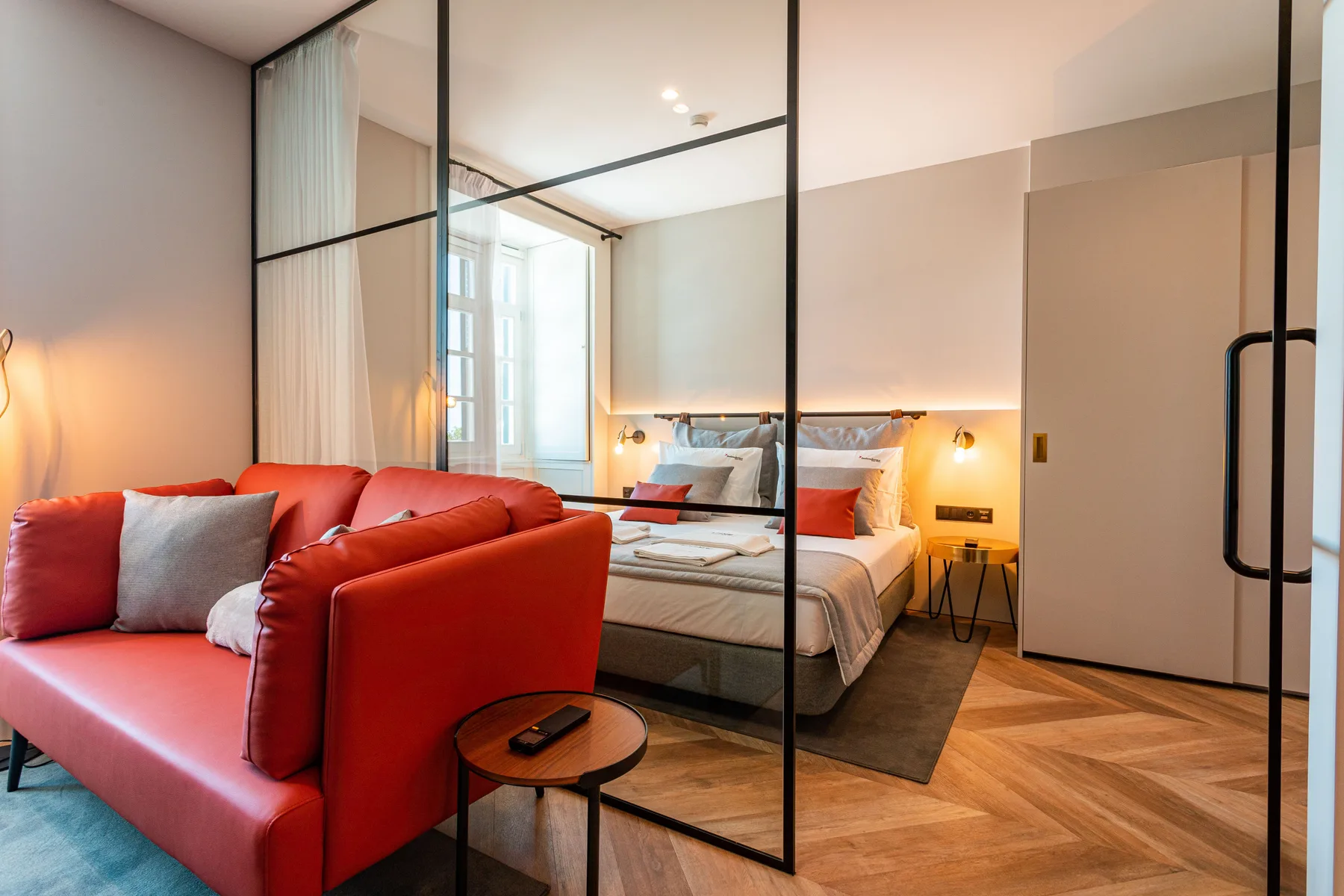 Dormitorio con cama, asientos rojos y paredes divisorias de vidrio.