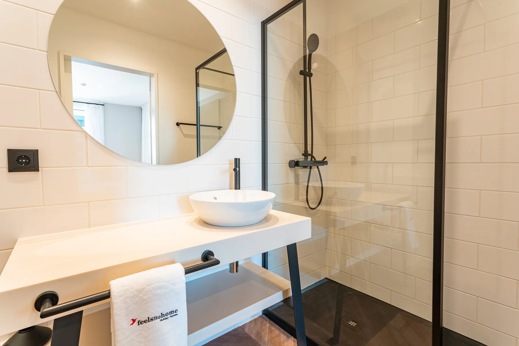 A tiled bathroom with a wall-mounted sink, round mirror, and shower.