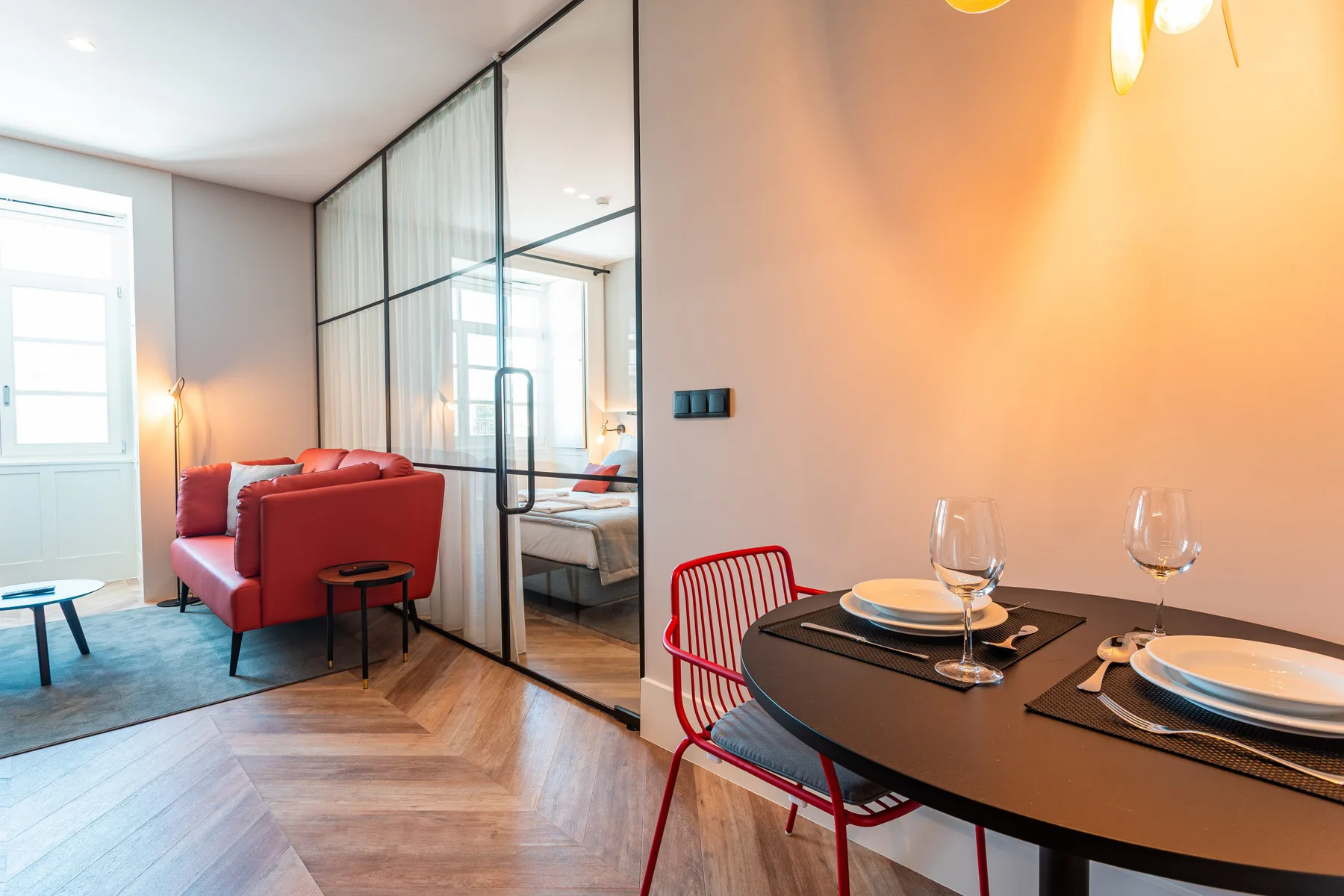 Comedor con la mesa puesta y asientos rojos junto a un tabique de vidrio.