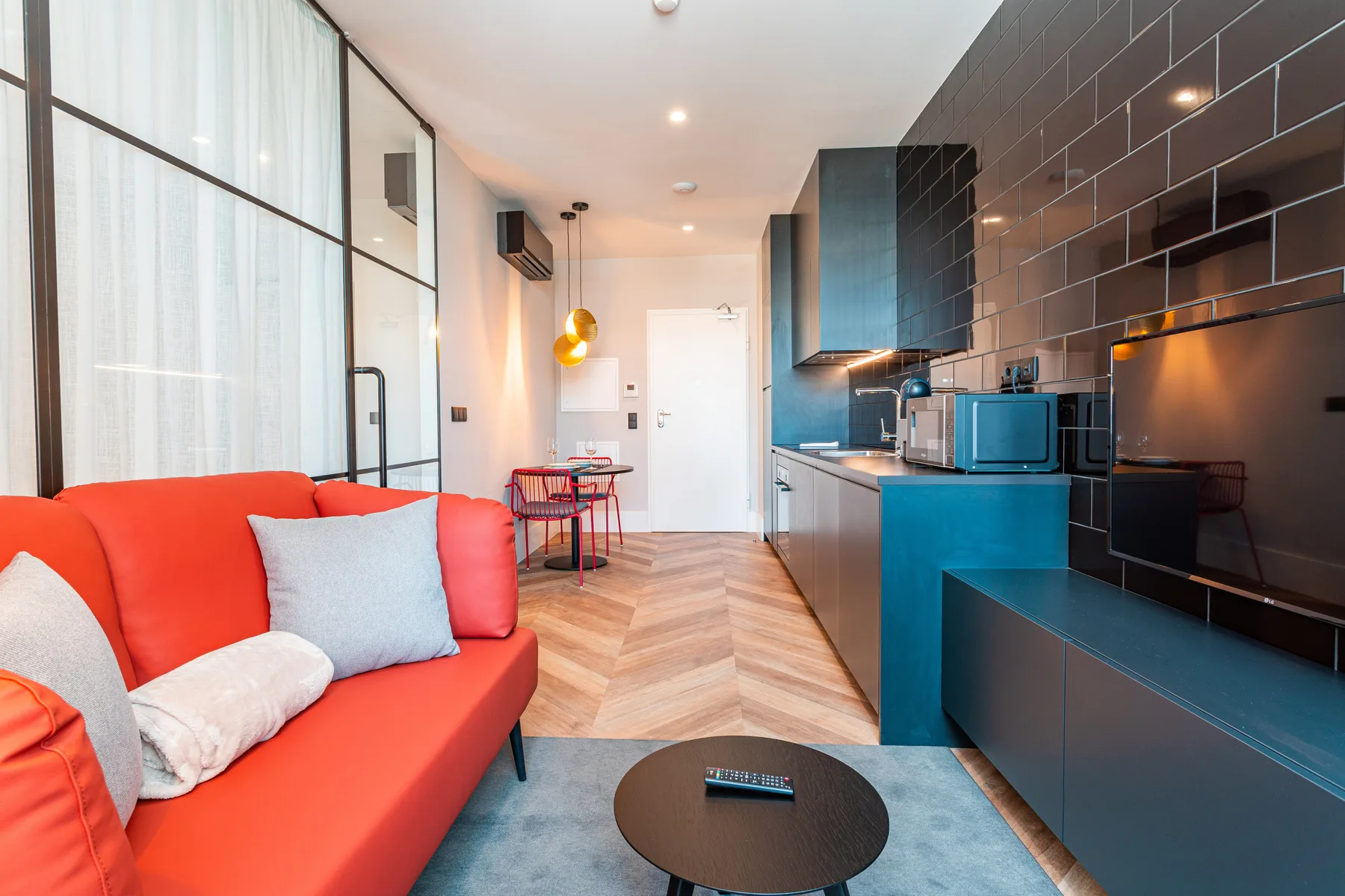 Una pequeña sala de estar diáfana con asientos coloridos, una mesa de comedor y cocina.