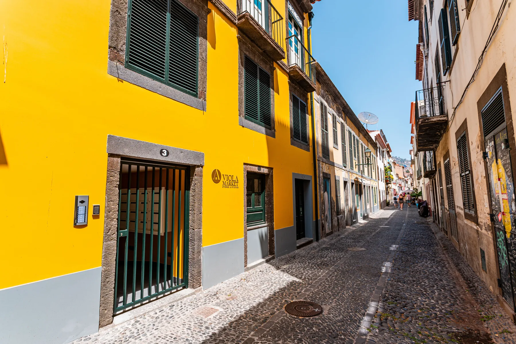Una estrecha calle adoquinada transcurre entre edificios coloridos bajo el sol.
