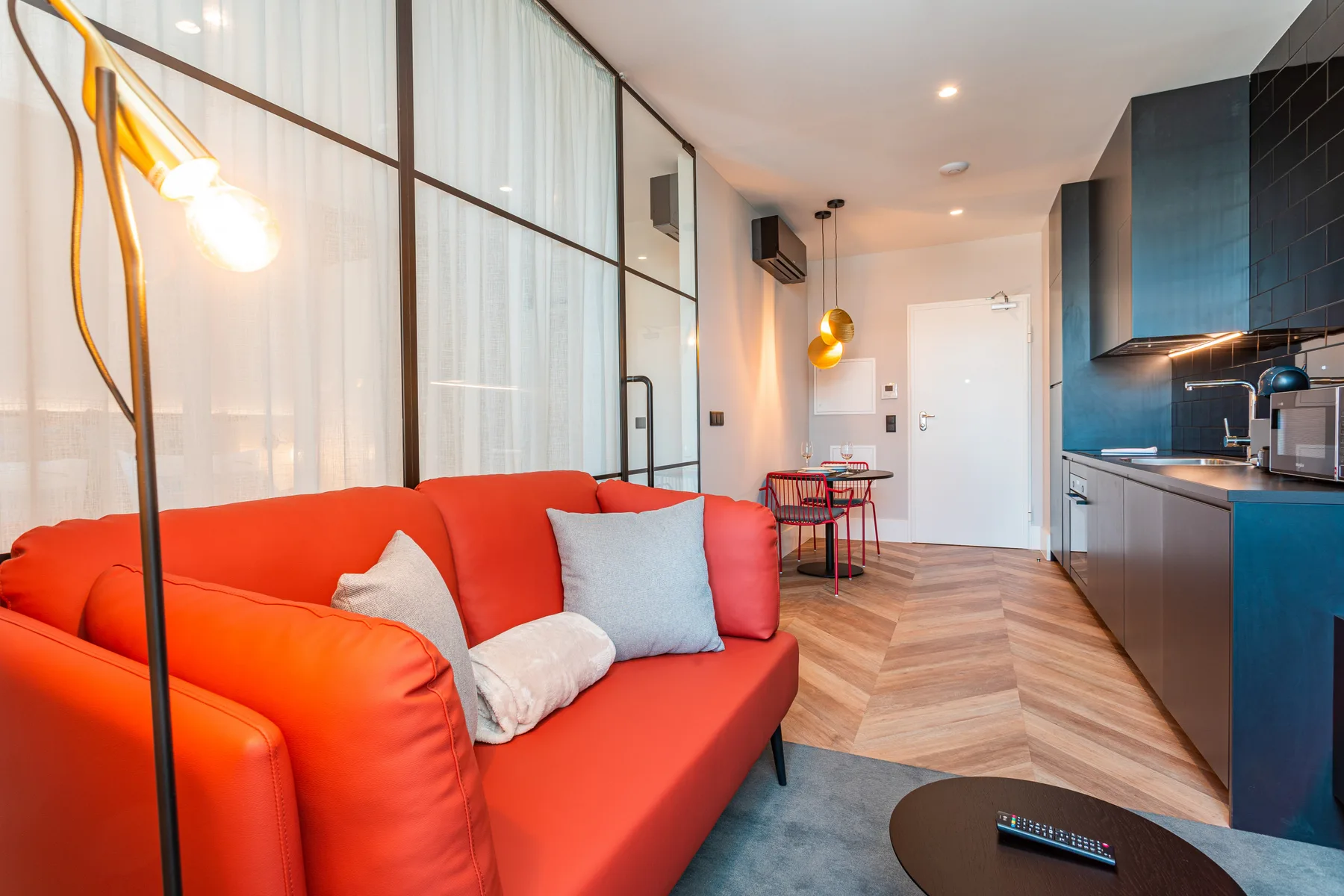 Una sala de estar moderna con asientos coloridos junto a una cocina abierta y una mesa de comedor.