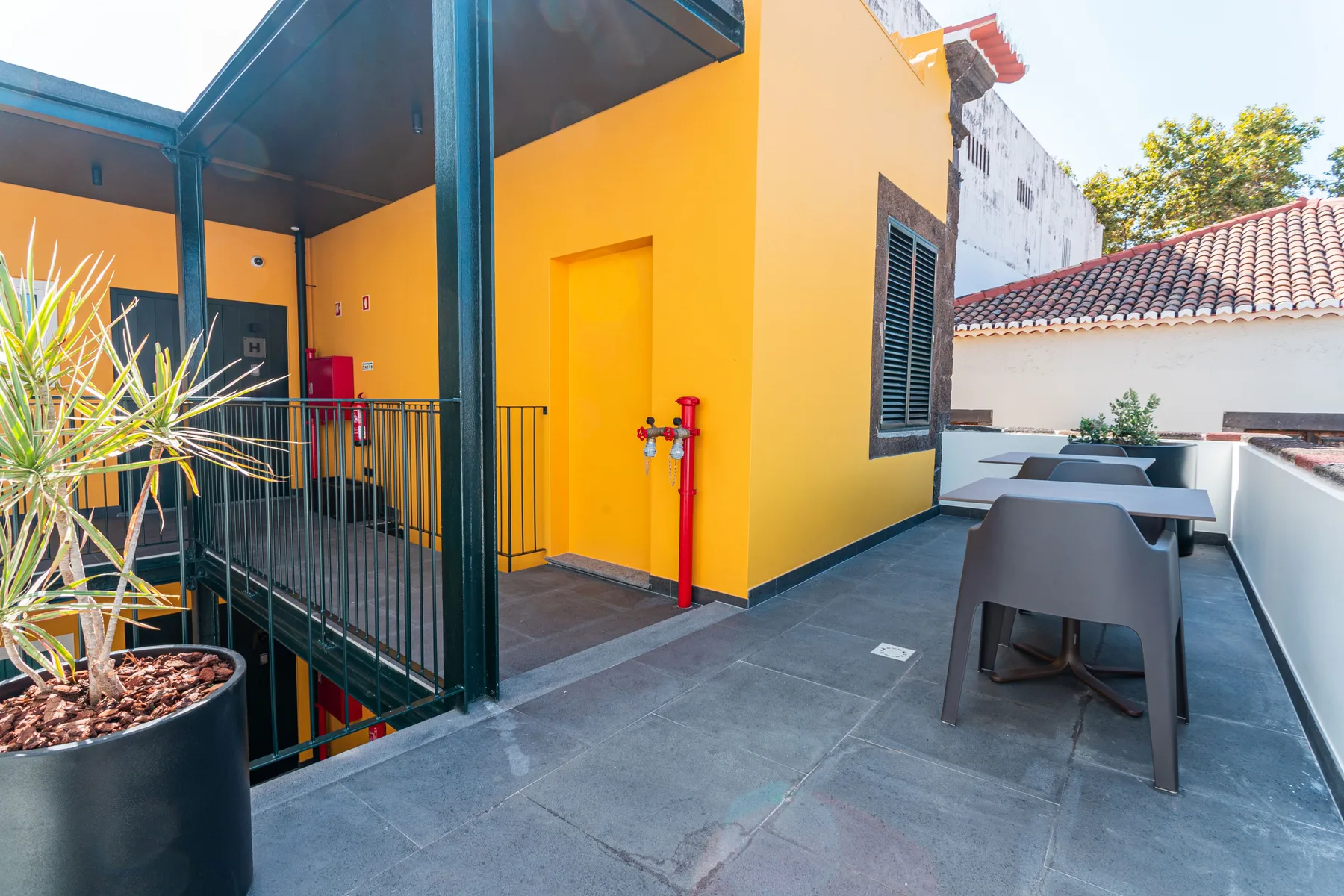 A rooftop terrace with outdoor seating beside a bright yellow building.