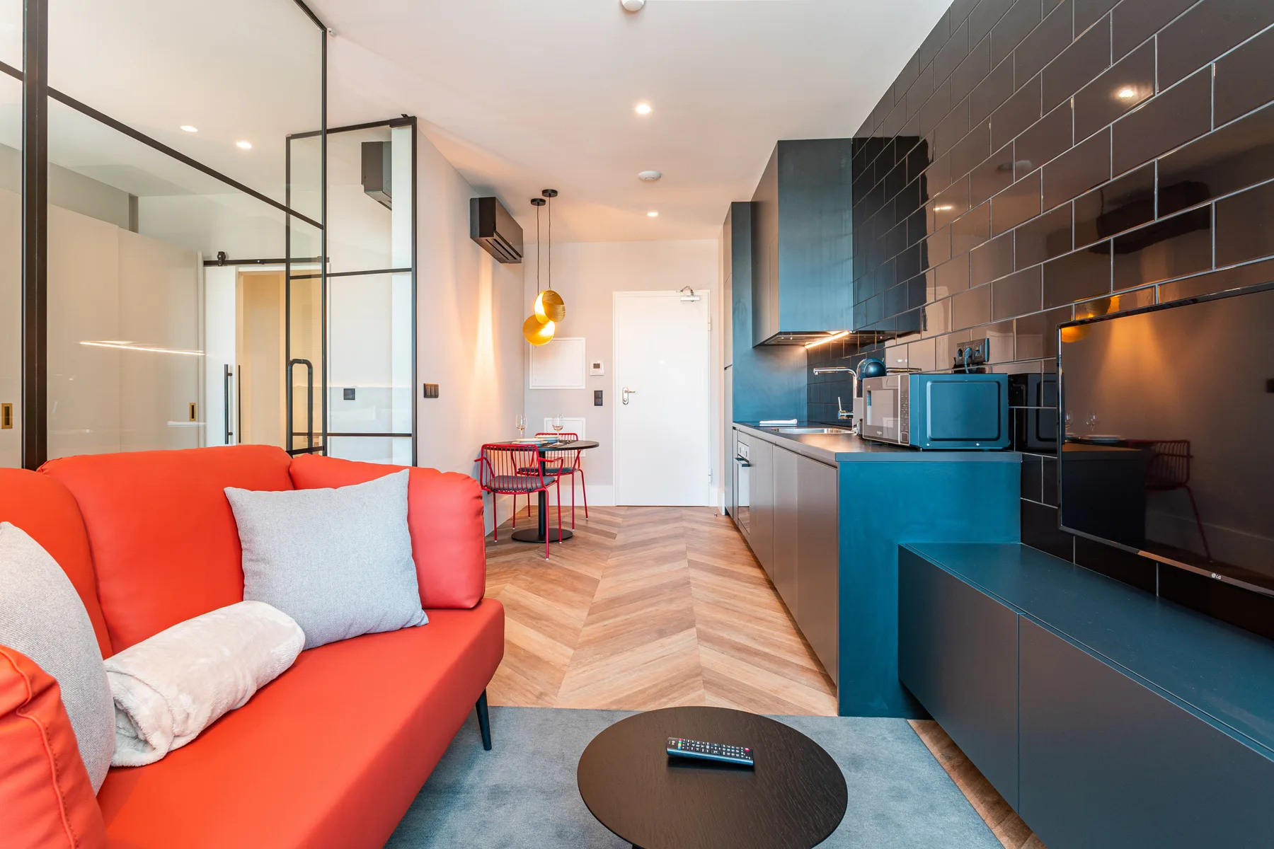 Una sala de estar diáfana tiene asientos rojos junto a una cocina compacta y una mesa de comedor.