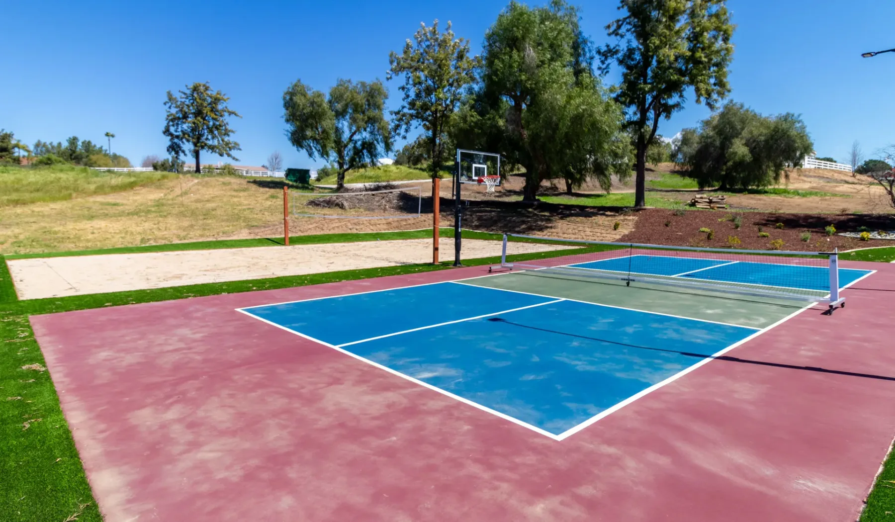 Outdoor sports courts with blue playing surfaces, surrounded by grass and trees.