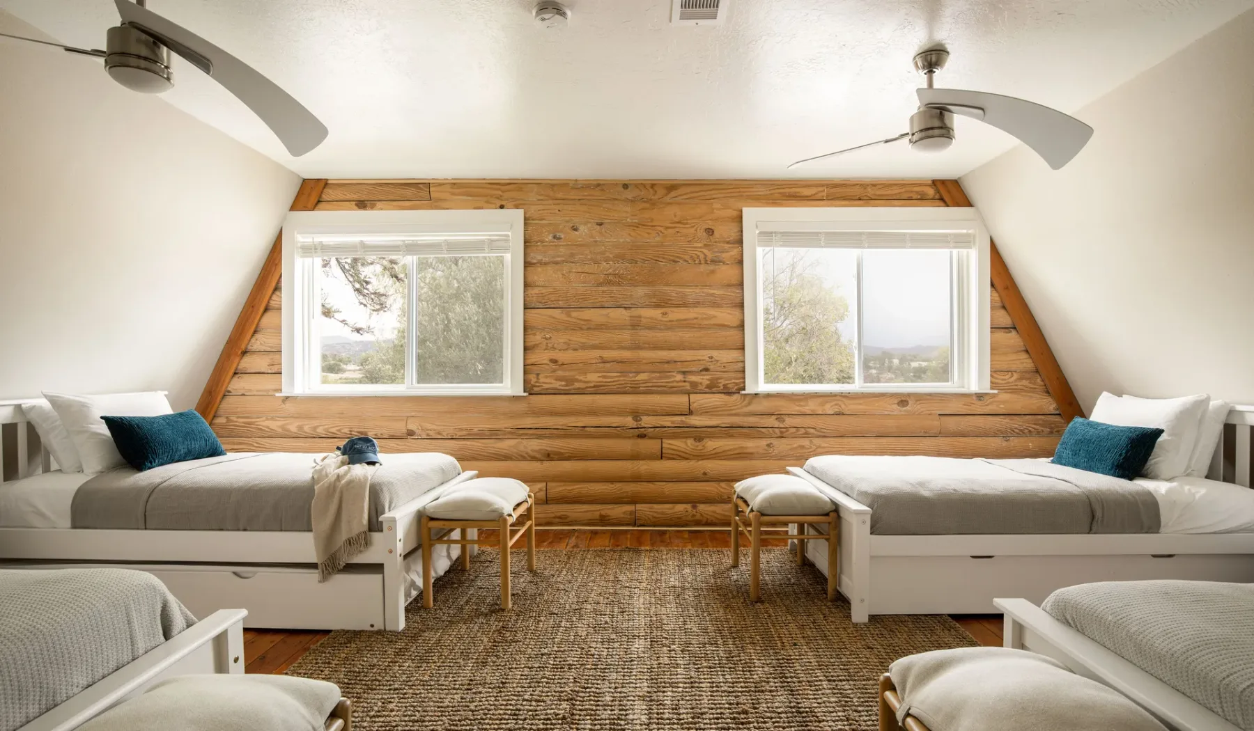 A bedroom with several beds, wood-paneled walls, and two windows.