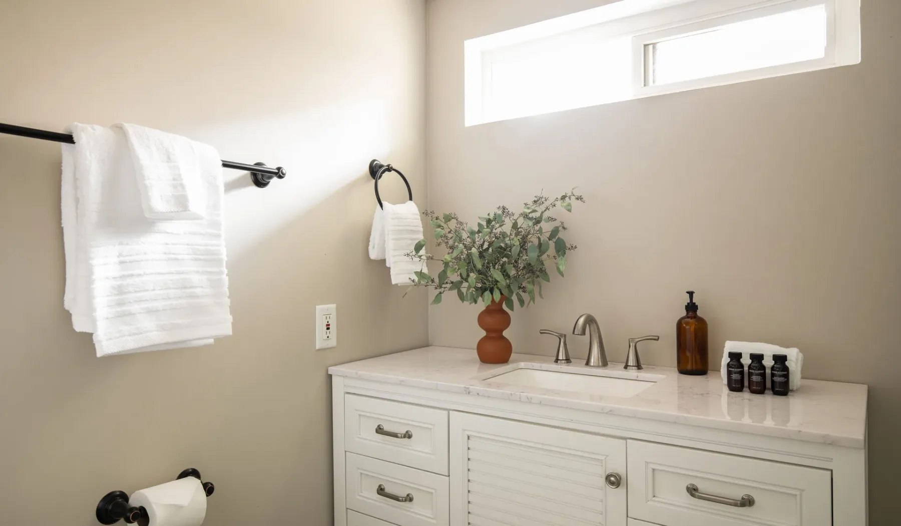 A bathroom vanity with a sink, towels, and a vase of greenery.