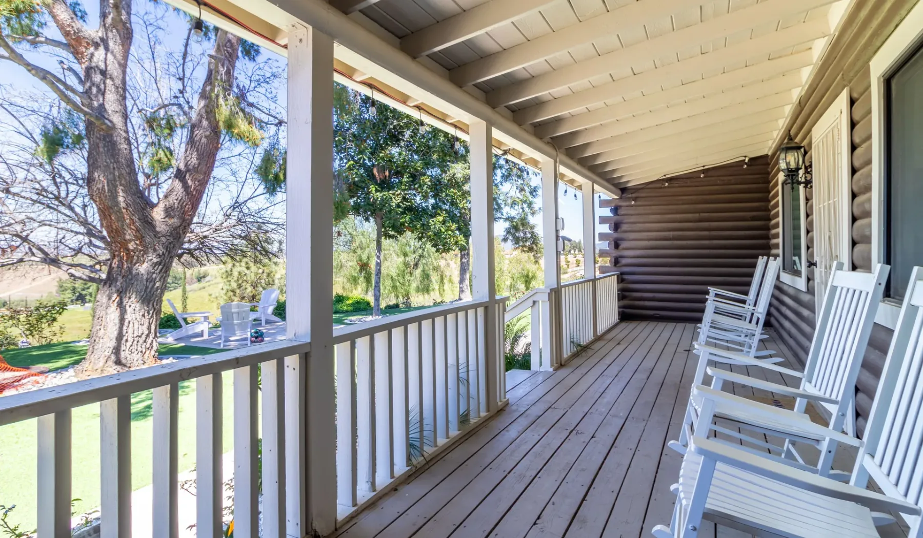 A covered porch with white railings and rocking chairs overlooks a leafy yard.