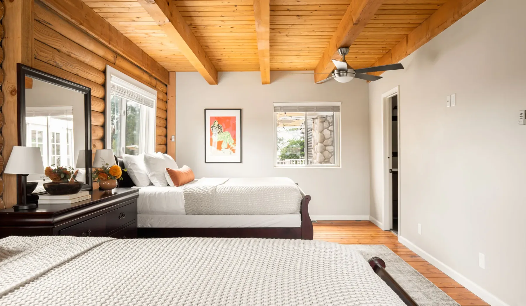 A bright bedroom with a bed, wooden ceiling, and windows.