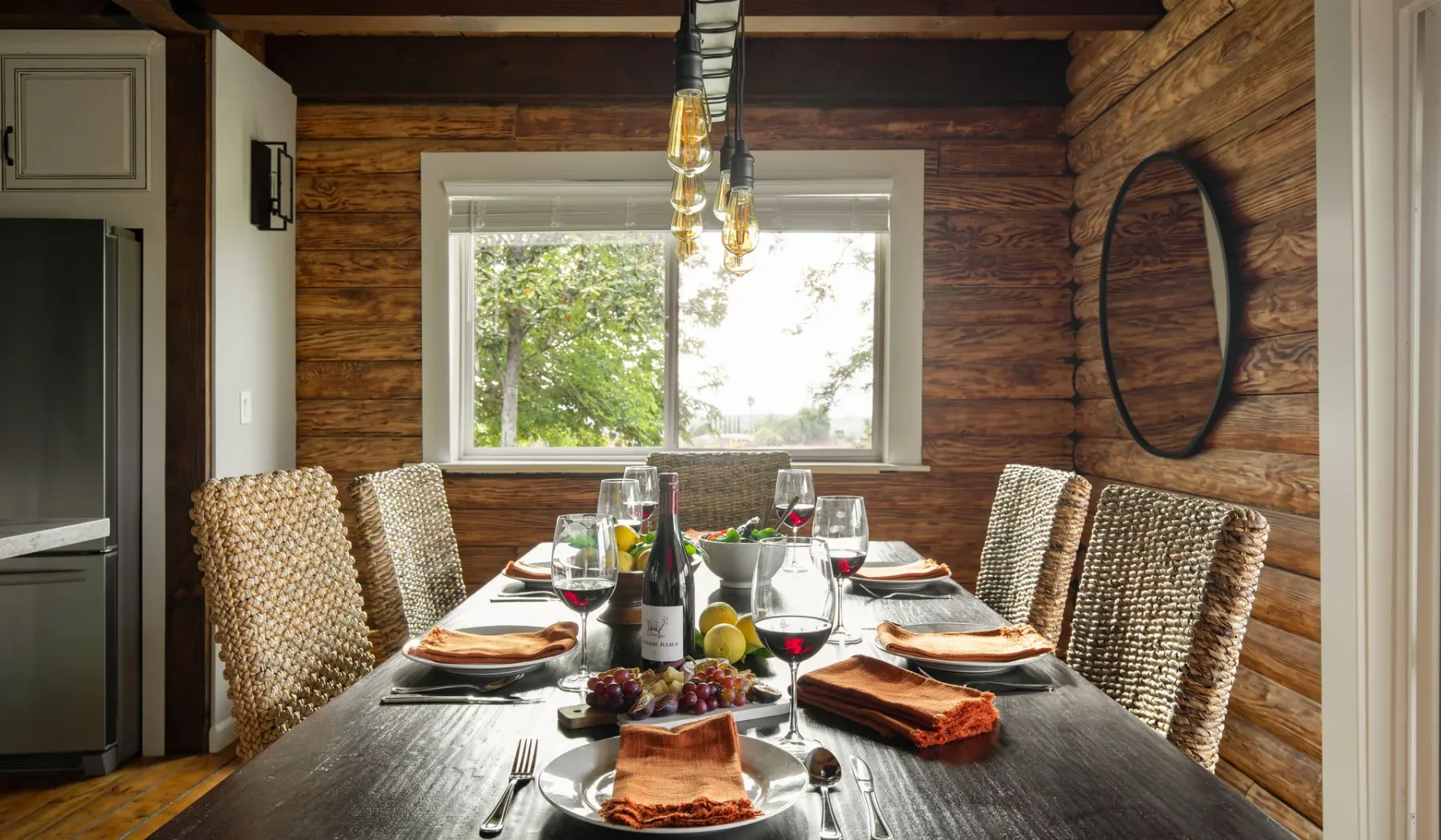 A dining room with a long table set for a meal beside a window.