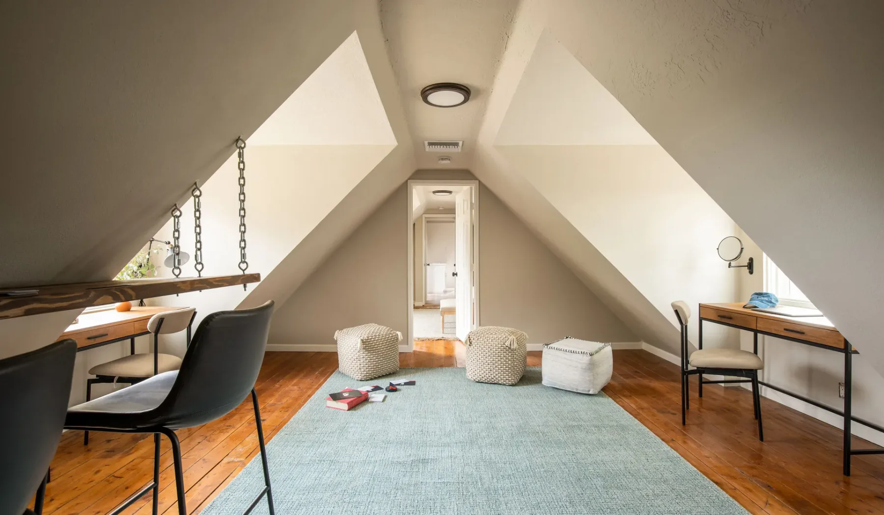 A bright attic room with a blue rug and desks beneath sloped ceilings.