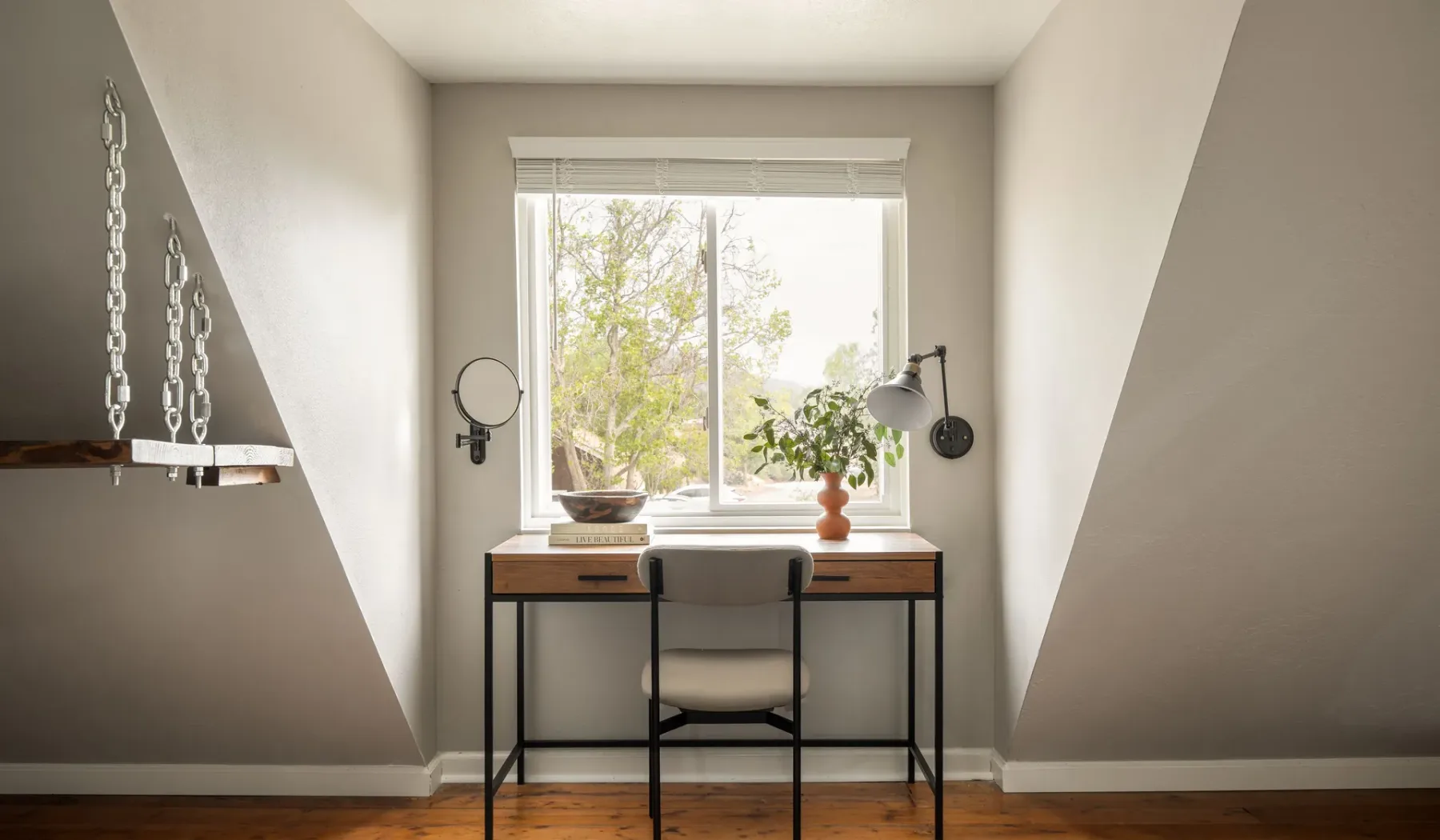 A desk and chair sit beneath a large window in a bright room.