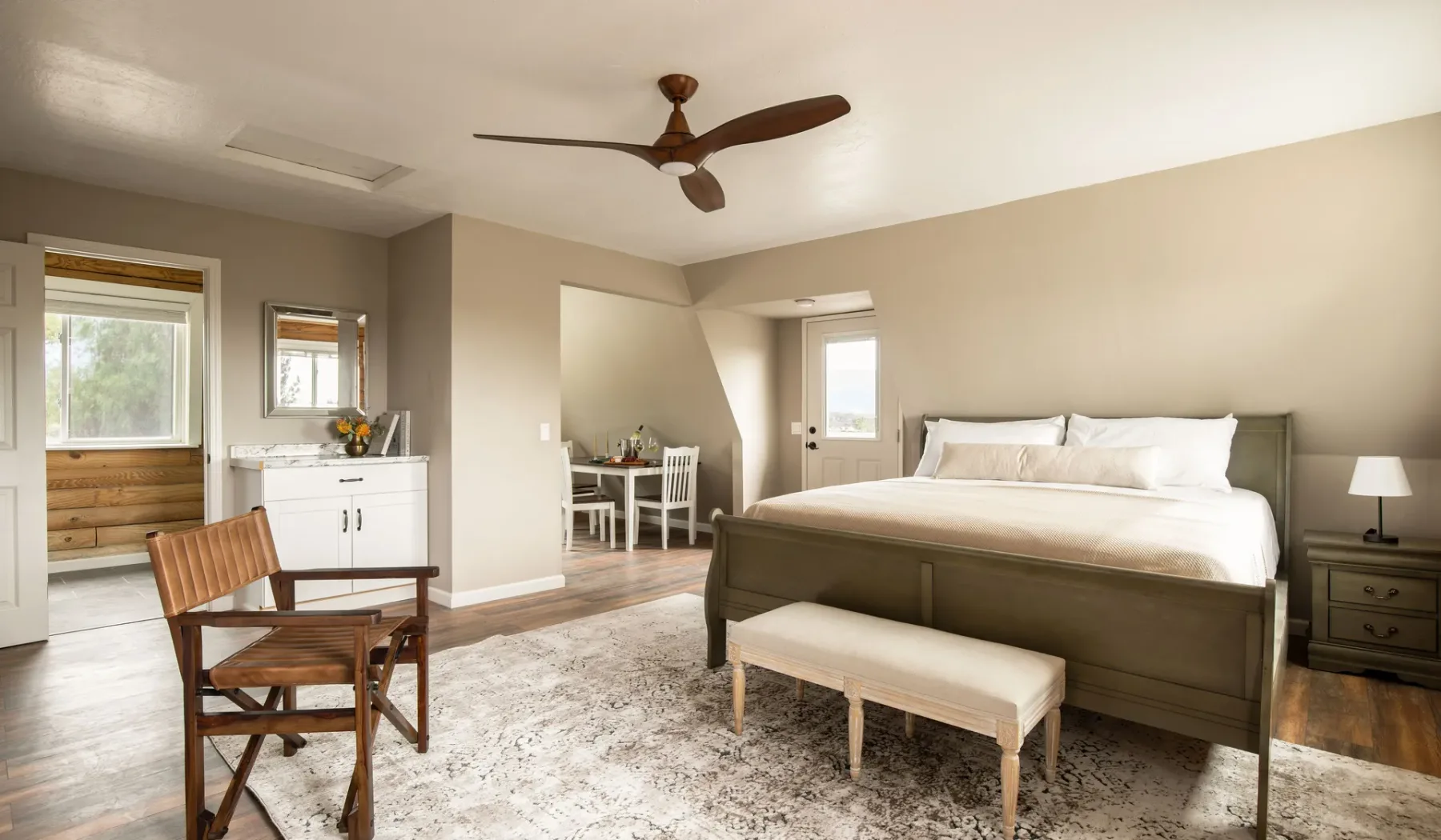 A bedroom with a large bed, a bench, and a small dining area.