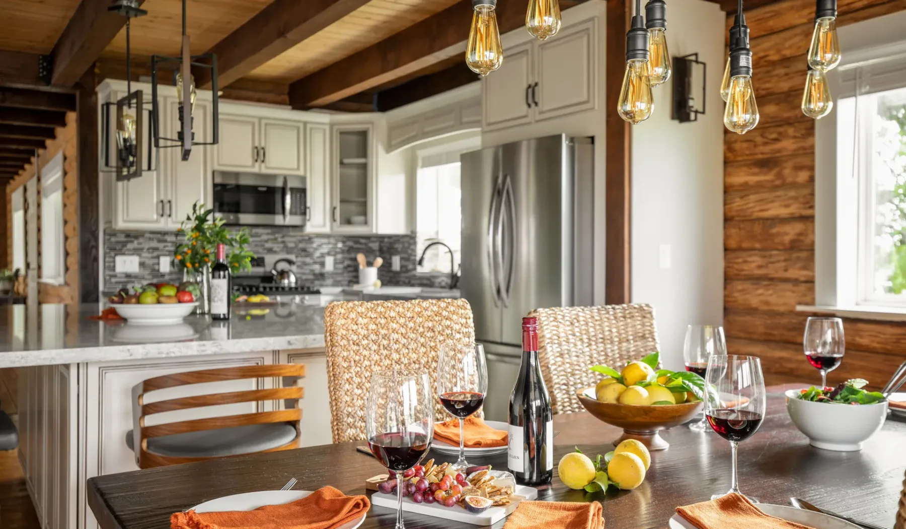 A dining table sits in a bright kitchen with a fruit bowl and pendant lights.