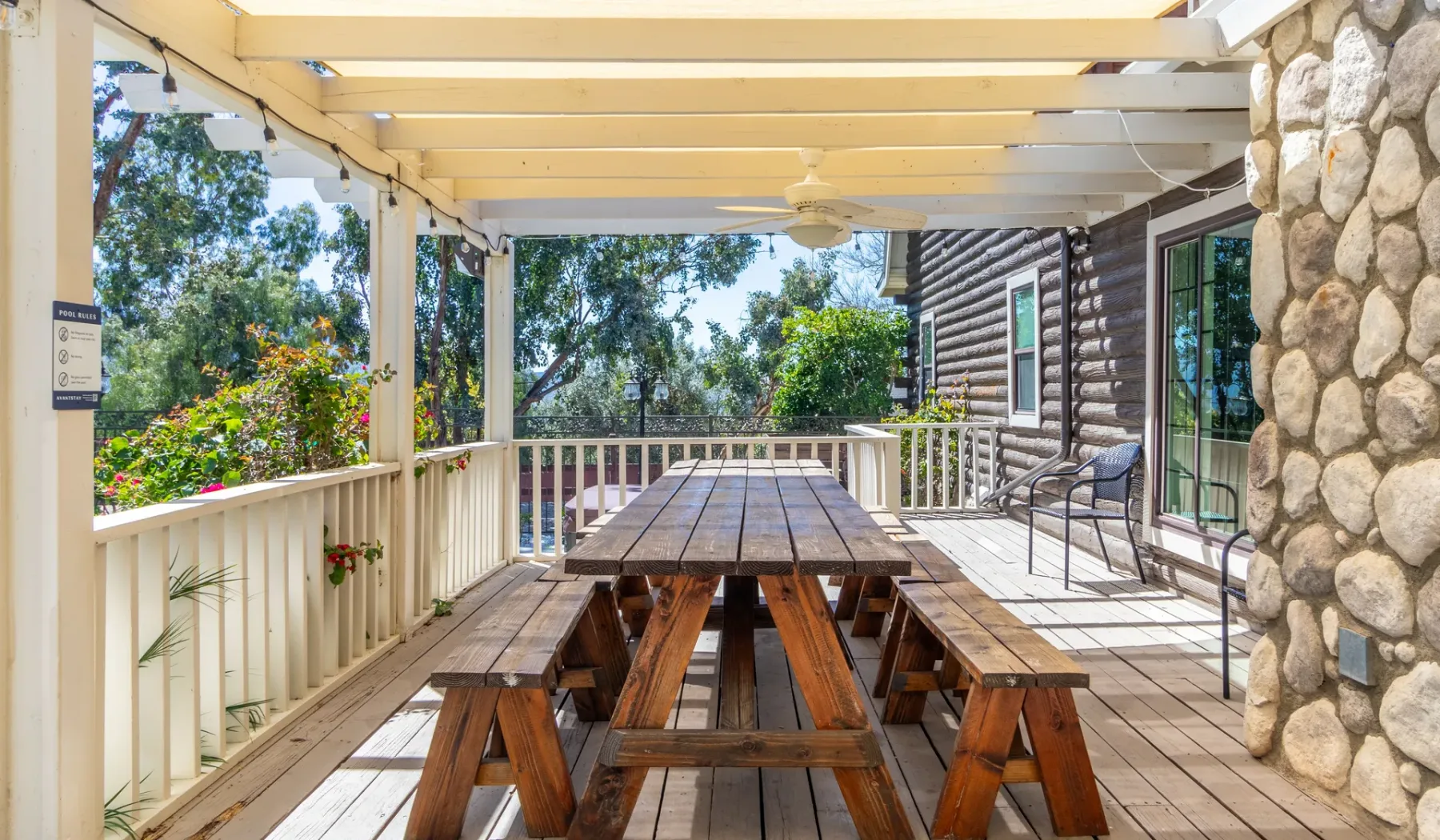 A covered outdoor dining deck with a long wooden picnic table and surrounding greenery.