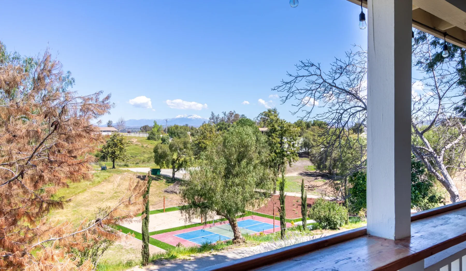 A covered balcony overlooks a colorful outdoor sports court and green grounds.