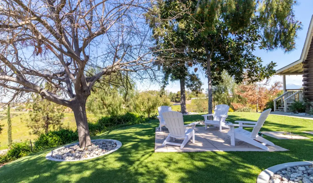 A shaded garden seating area with white chairs arranged on a patio.