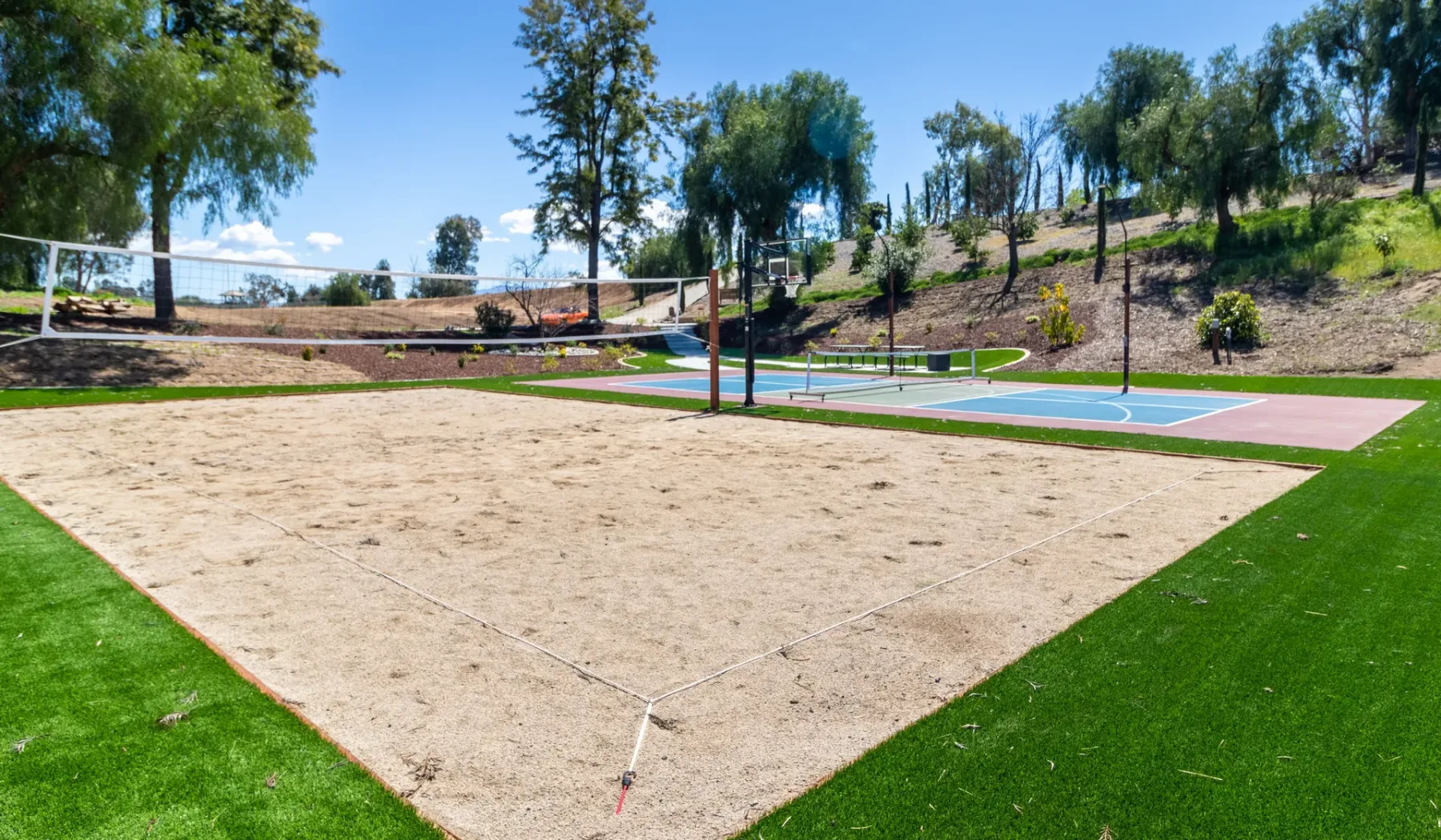 An outdoor sand volleyball court beside a painted sports court.