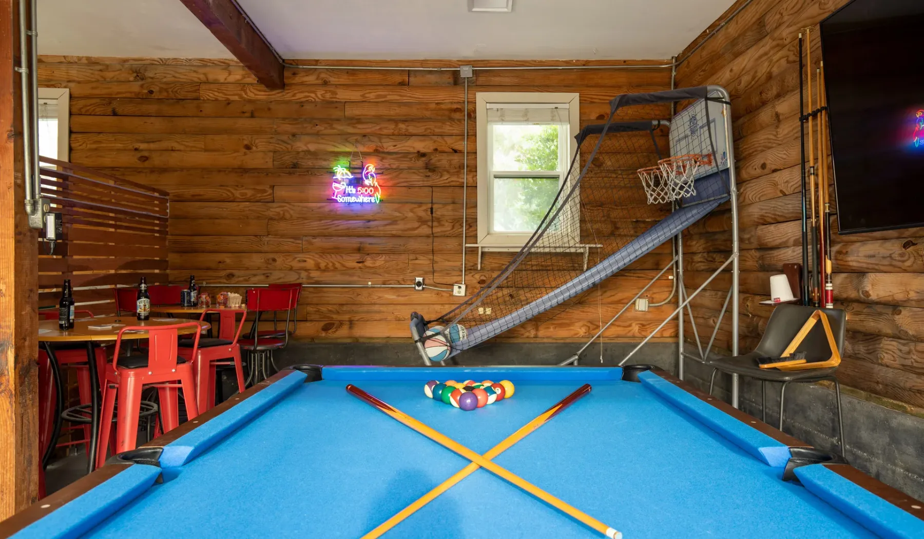A game room with a blue pool table and a basketball hoop.