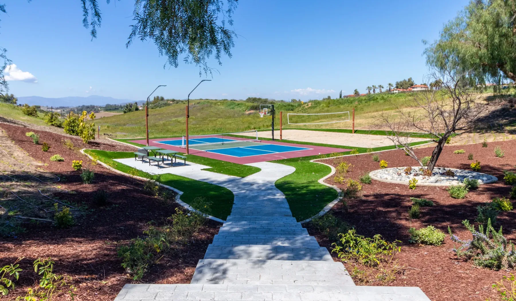 A landscaped outdoor recreation area with a colorful court and paved walkway.